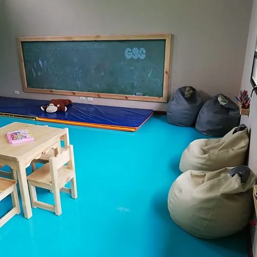 Salón de preescolar con tablero, colchonetas y puffs de lectura