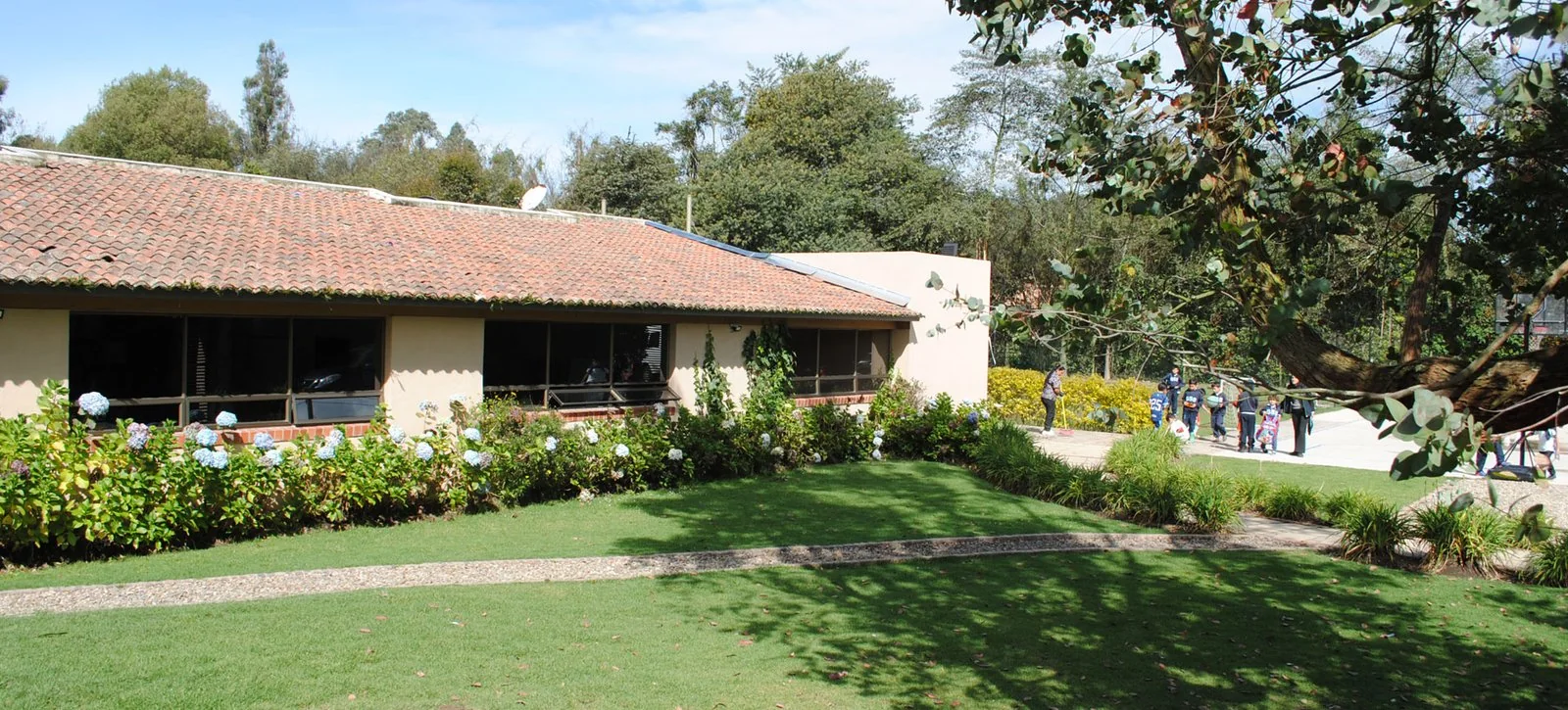 Sede Cajicá: salones de teja rodeados de jardín con hortensias, prado y estudiantes al fondo