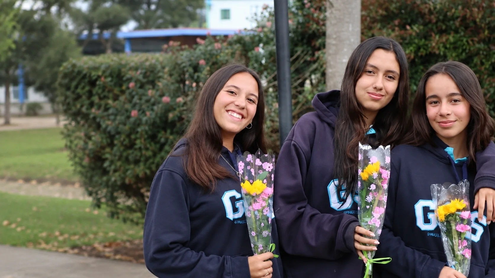 Tres estudiantes del Gimnasio Santamaría de la Sabana sonriendo con flores en la mano