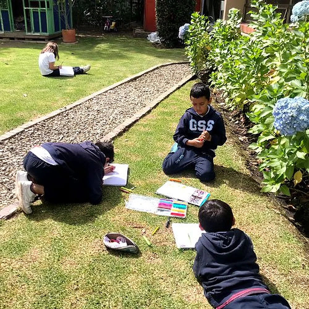 Estudiantes trabajando en sus cuadernos sobre el prado del colegio