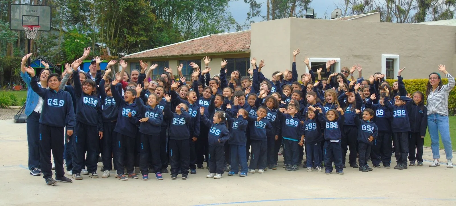 Estudiantes y docentes del colegio saludando con los brazos en alto en el patio