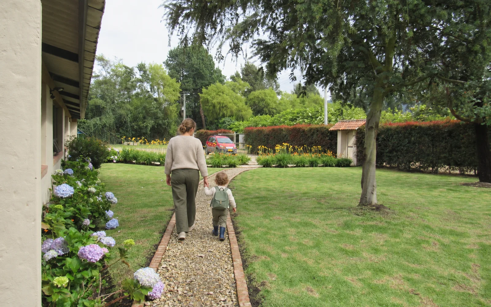 Una profesora y un niño de 2 años caminan de la mano por el sendero de hortensias de la sede Cajicá
