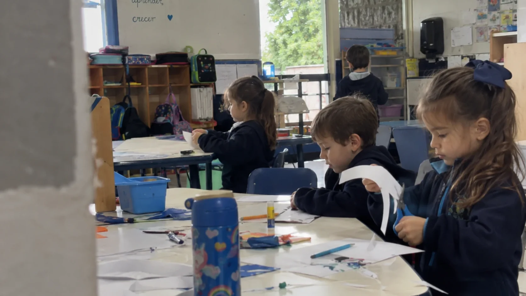 Niños de preescolar recortando y pegando papel en su mesa de trabajo, en el salón
